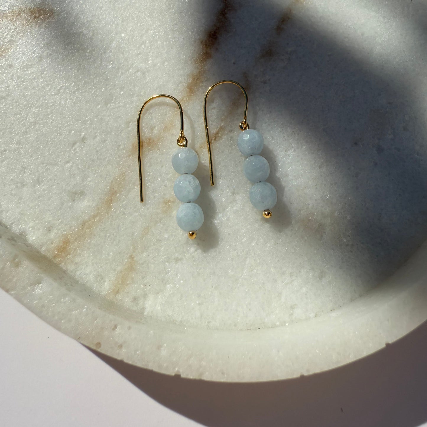 Pair of gold aquamarine bead earrings on a marble surface