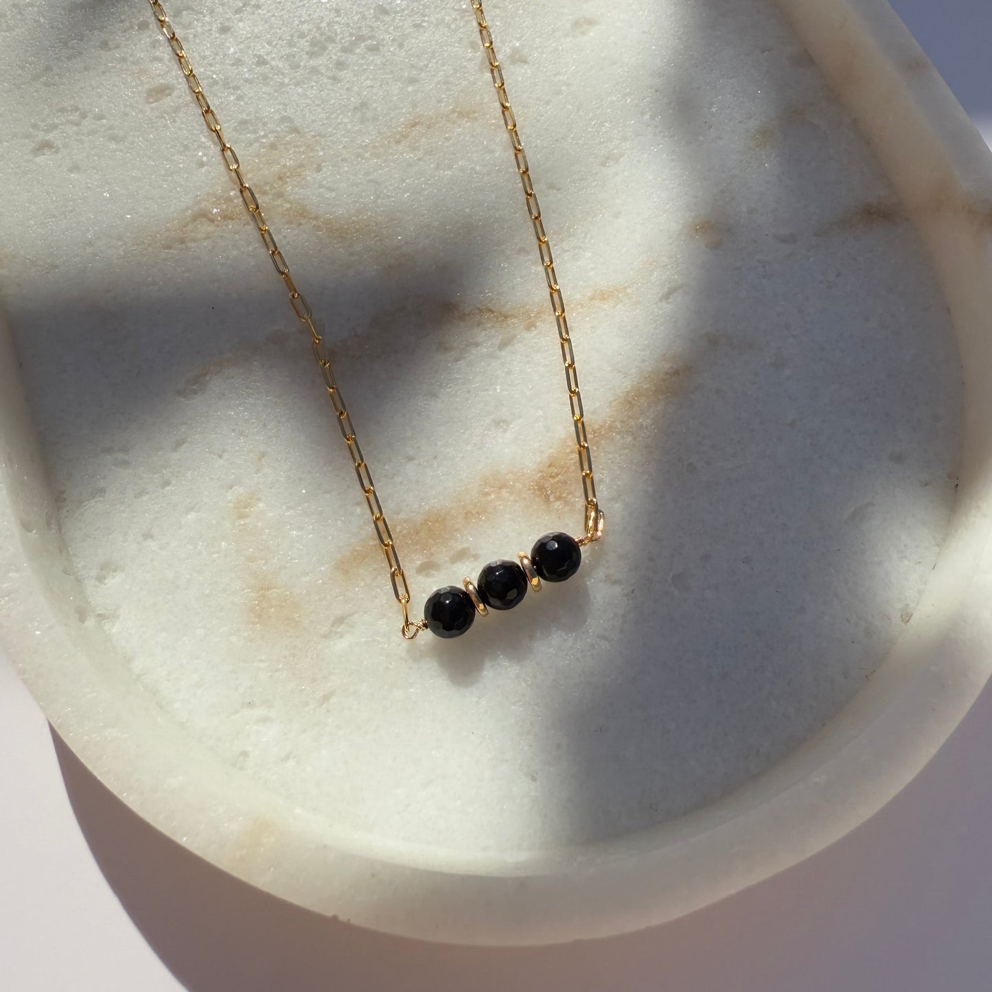 Gold necklace with black onyx beads on a marble surface