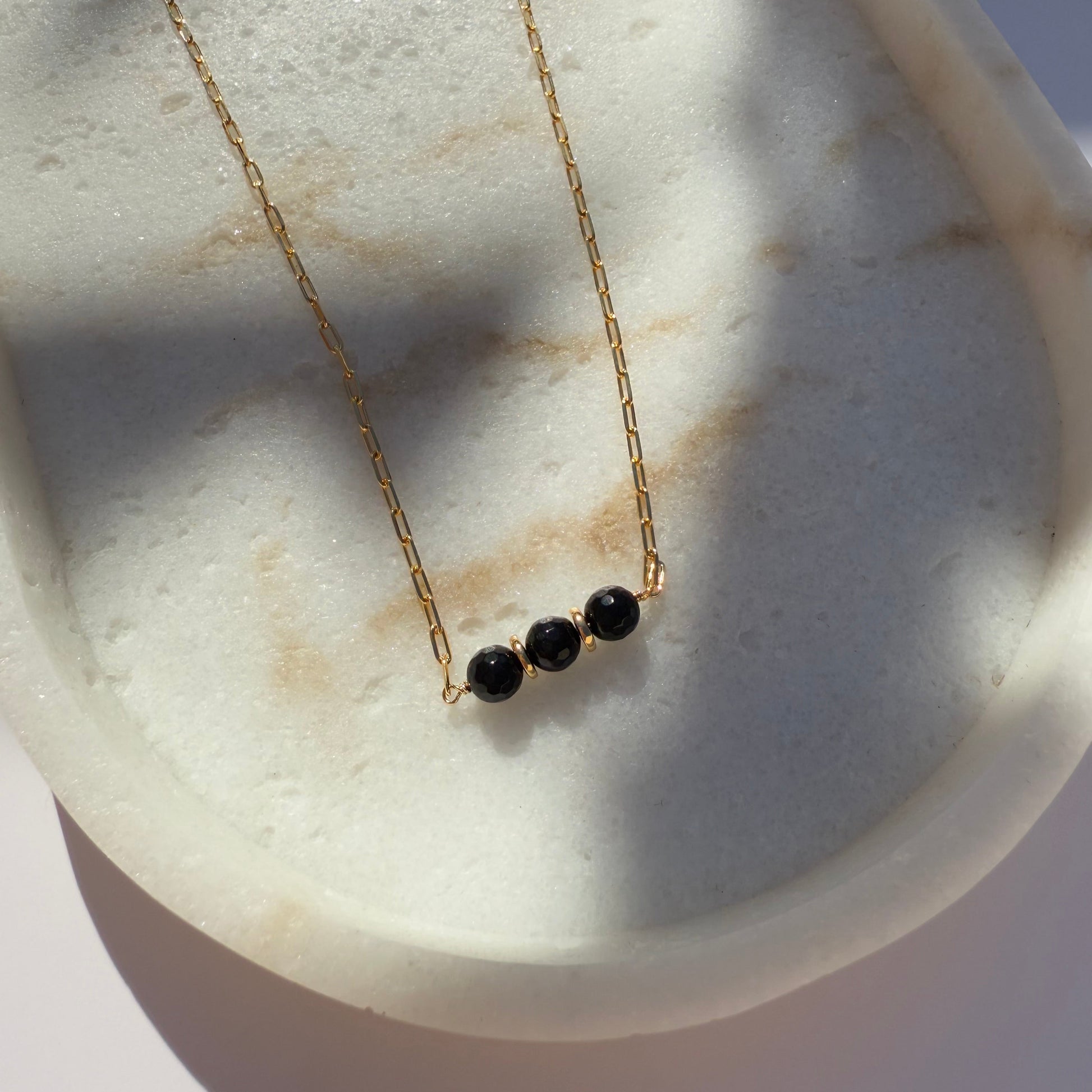 Gold necklace with black onyx beads on a marble surface