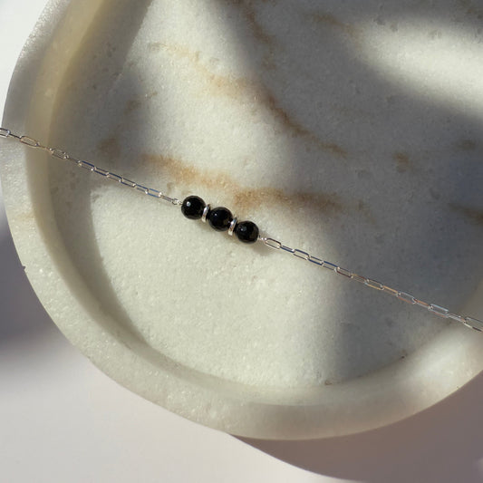 Silver necklace with black onyx beads on marble surface