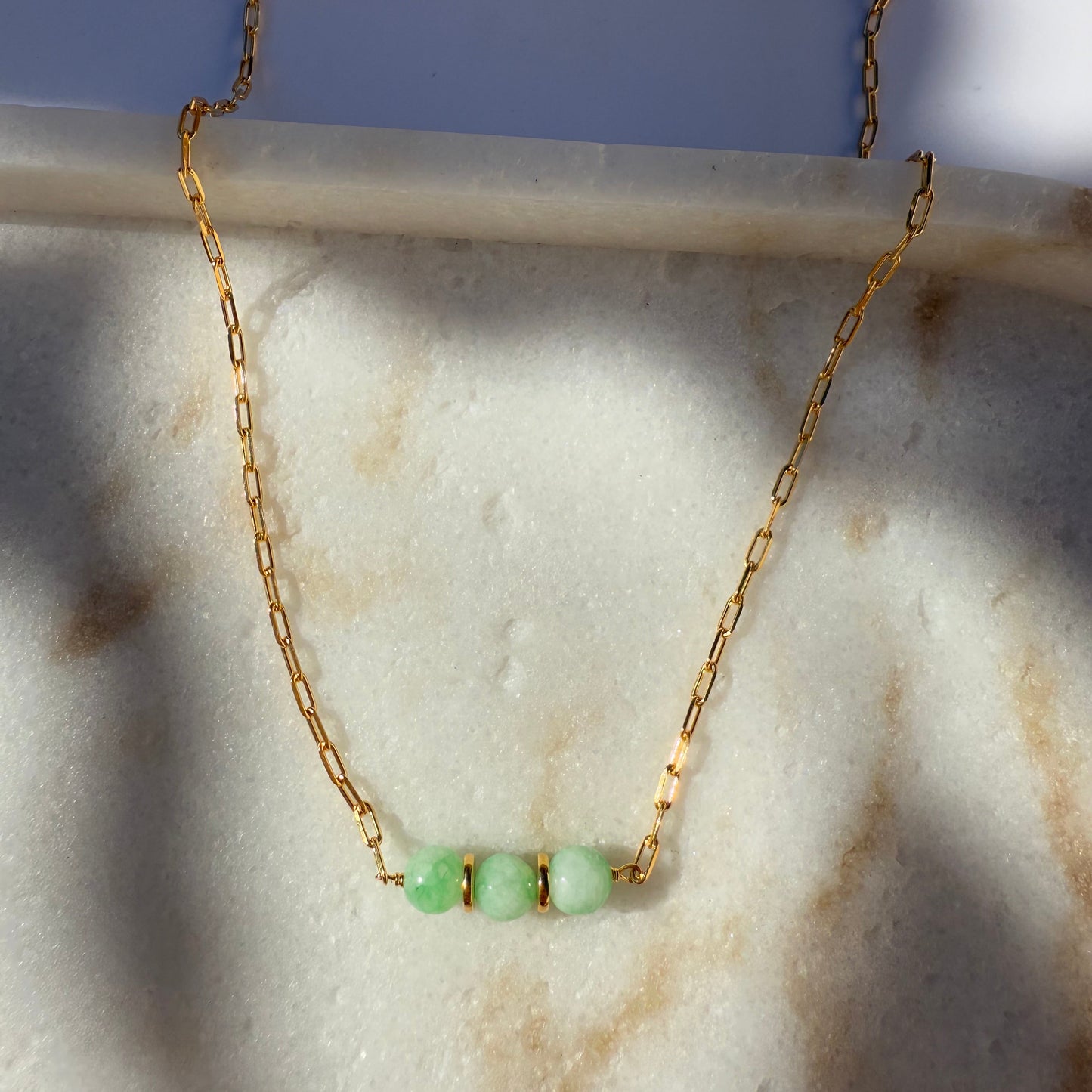 Gold necklace with chrysoprase beads on a marble surface