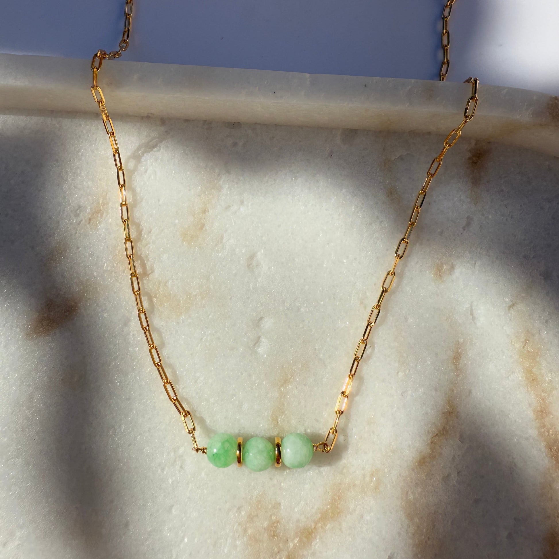 Gold necklace with chrysoprase beads on a marble surface