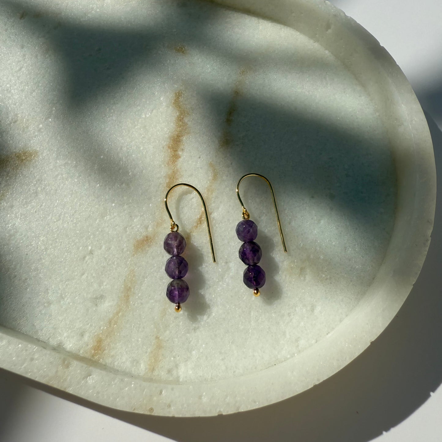 Pair of gold amethyst beaded earrings on a marble surface