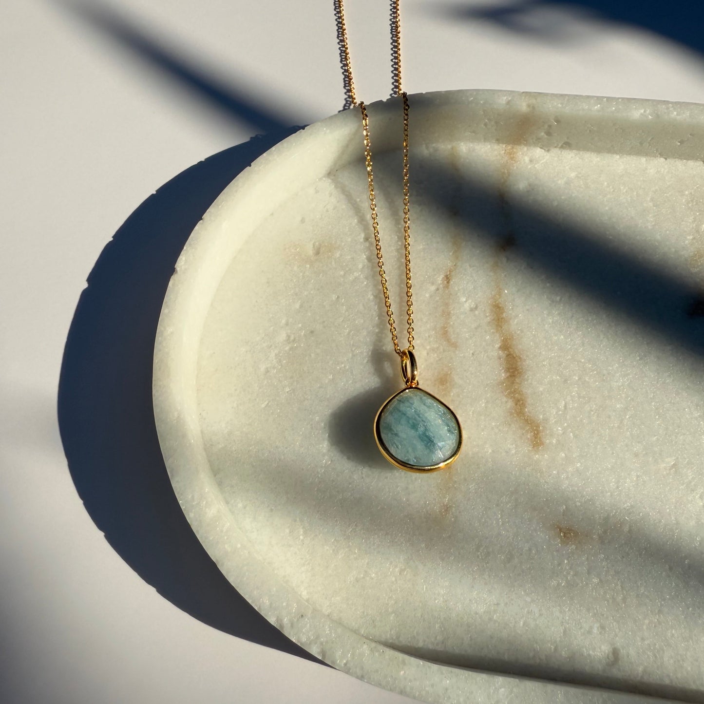 Gold aquamarine necklace with a pear pendant on a marble surface