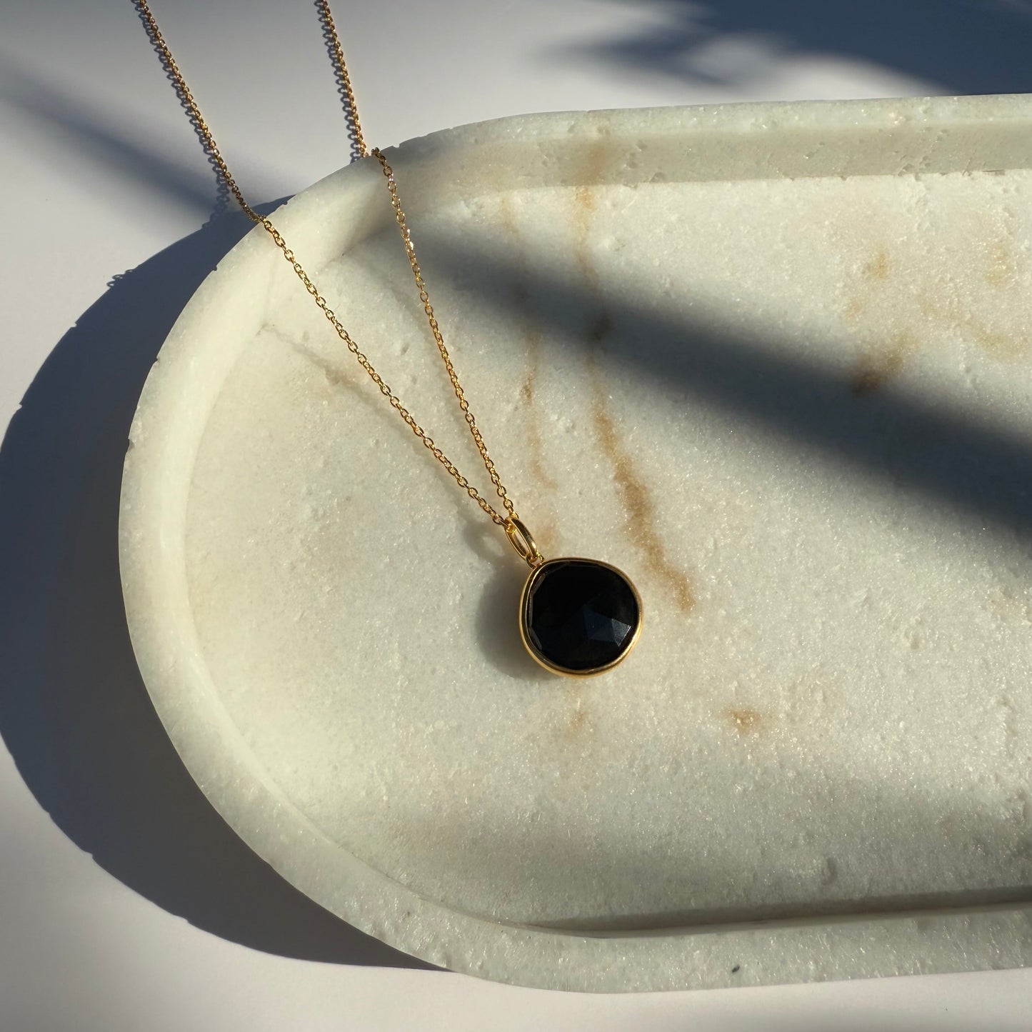 Gold black onyx necklace with a pear pendant on a marble surface