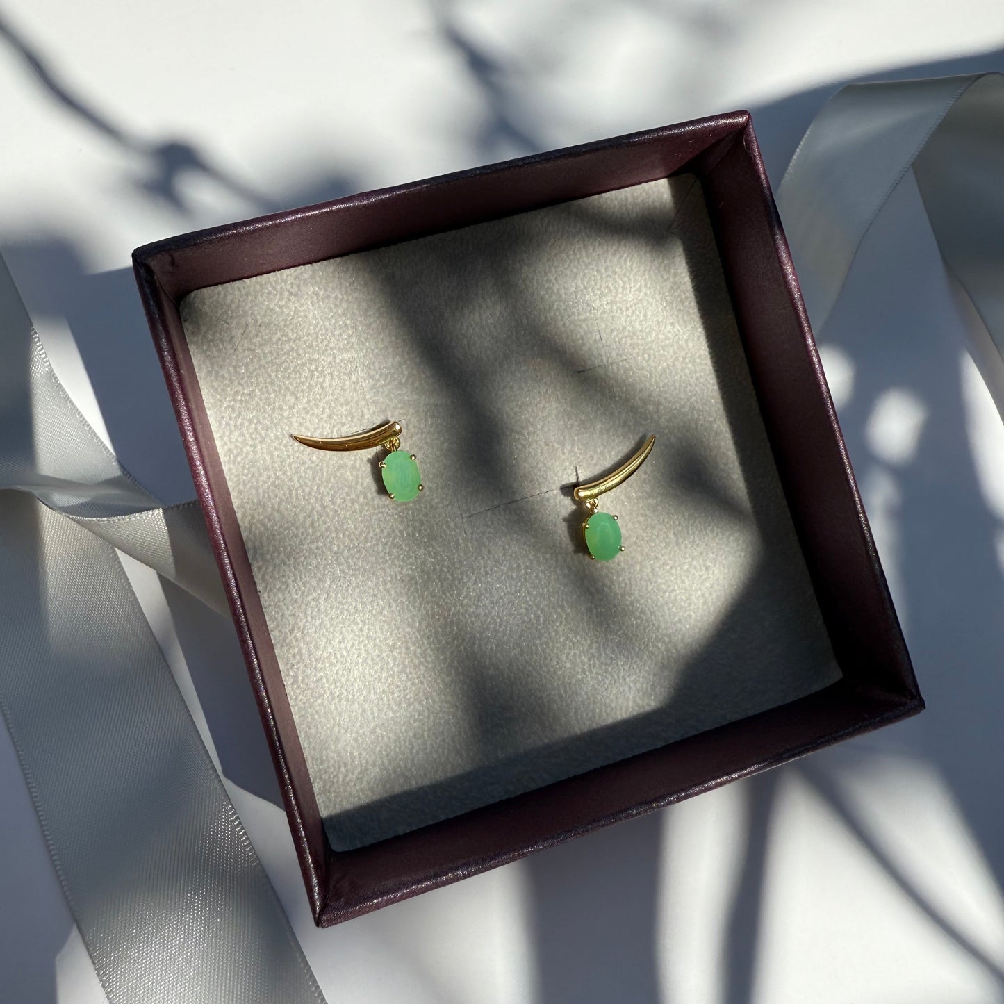 Pair of gold earrings with green chrysoprase stones in a jewelry box.