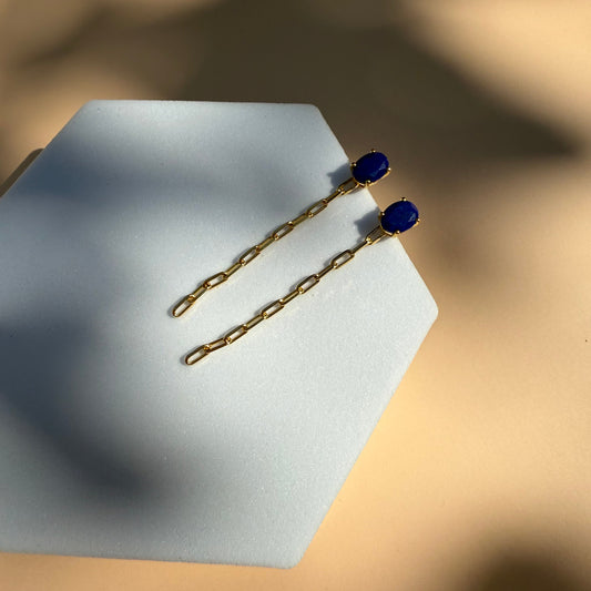 Gold lapis lazuli earrings with dangling chain on a white hexagon 