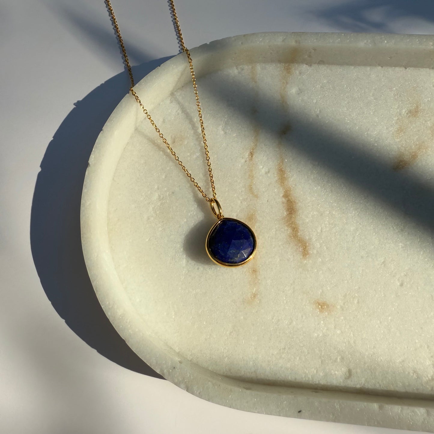 Gold lapis lazuli necklace with a pear pendant on a marble surface