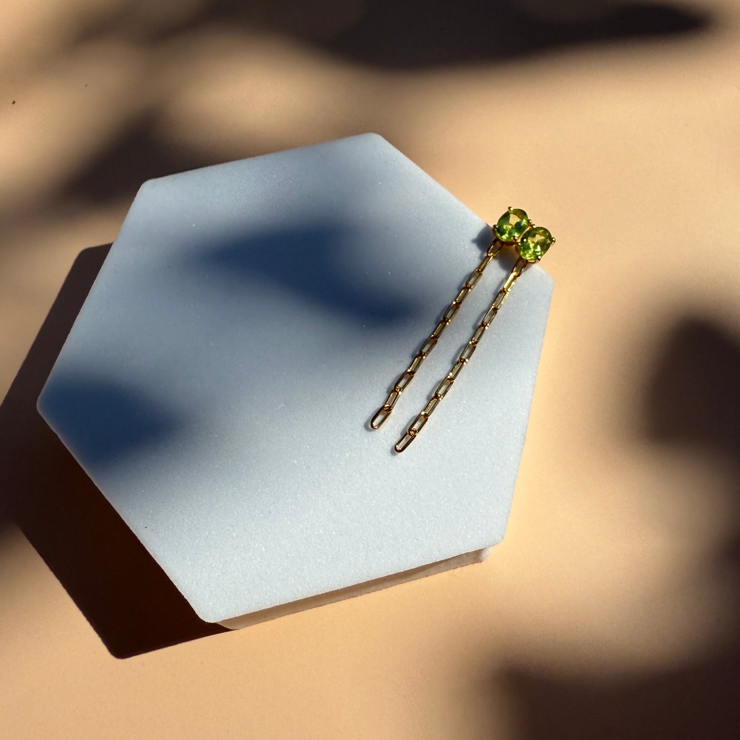 Gold peridot earrings with dangling chain on a white hexagon 