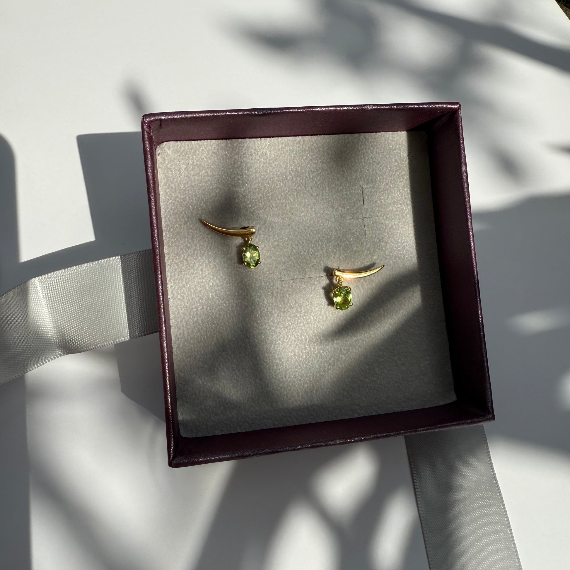 Pair of gold earrings with peridot gemstones in a jewelry box.