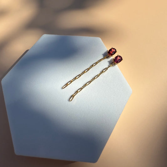 Gold rhodolite earrings with dangling chain on a white hexagon 