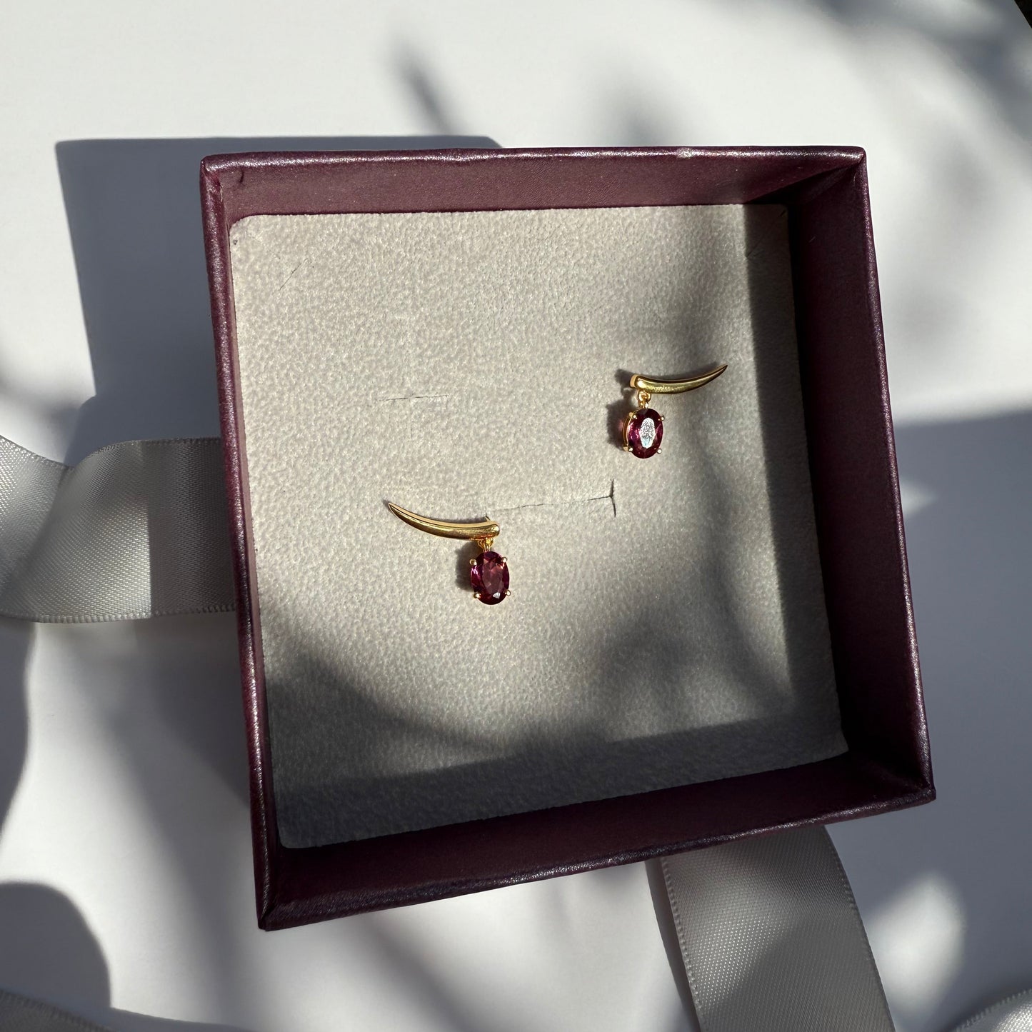 Pair of gold earrings with rhodolite gemstones in a jewelry box 