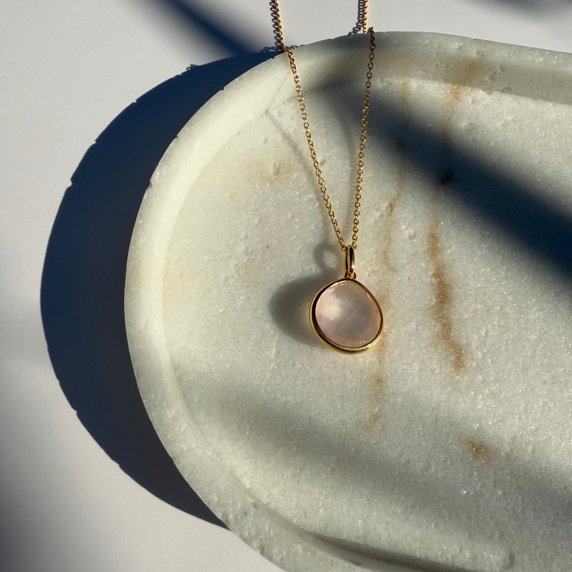 Gold rose quartz necklace with a pear pendant on a marble surface
