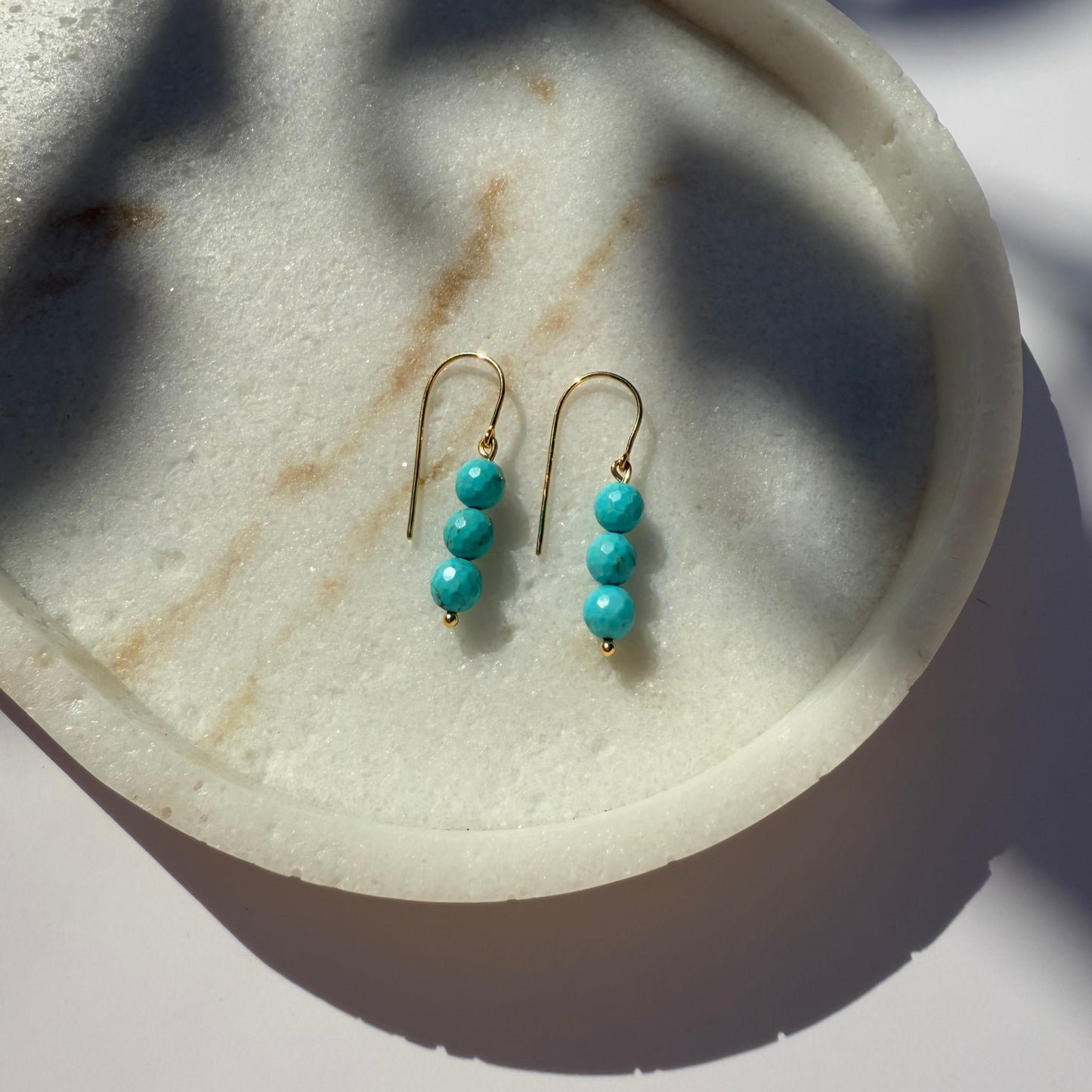 Turquoise gold beaded earrings on a marble surface