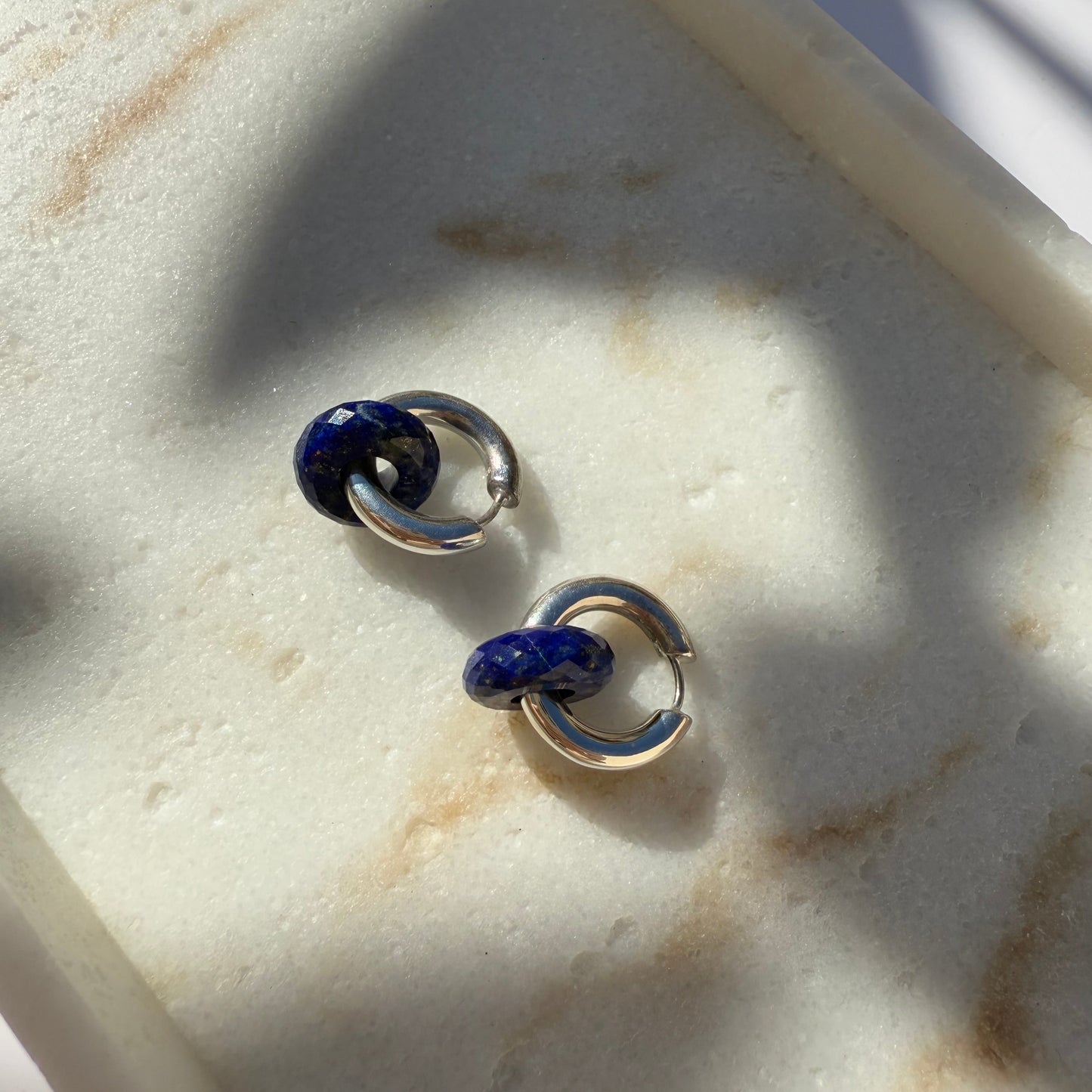 Pair of silver hoop earrings with lapis lazuli  on a marble surface