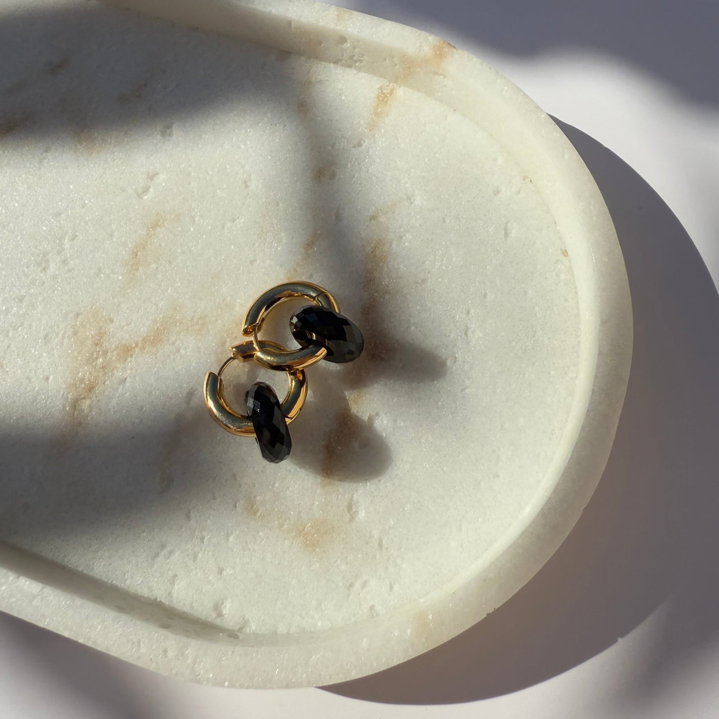 Pair of gold black onyx hoop earrings on marble stone