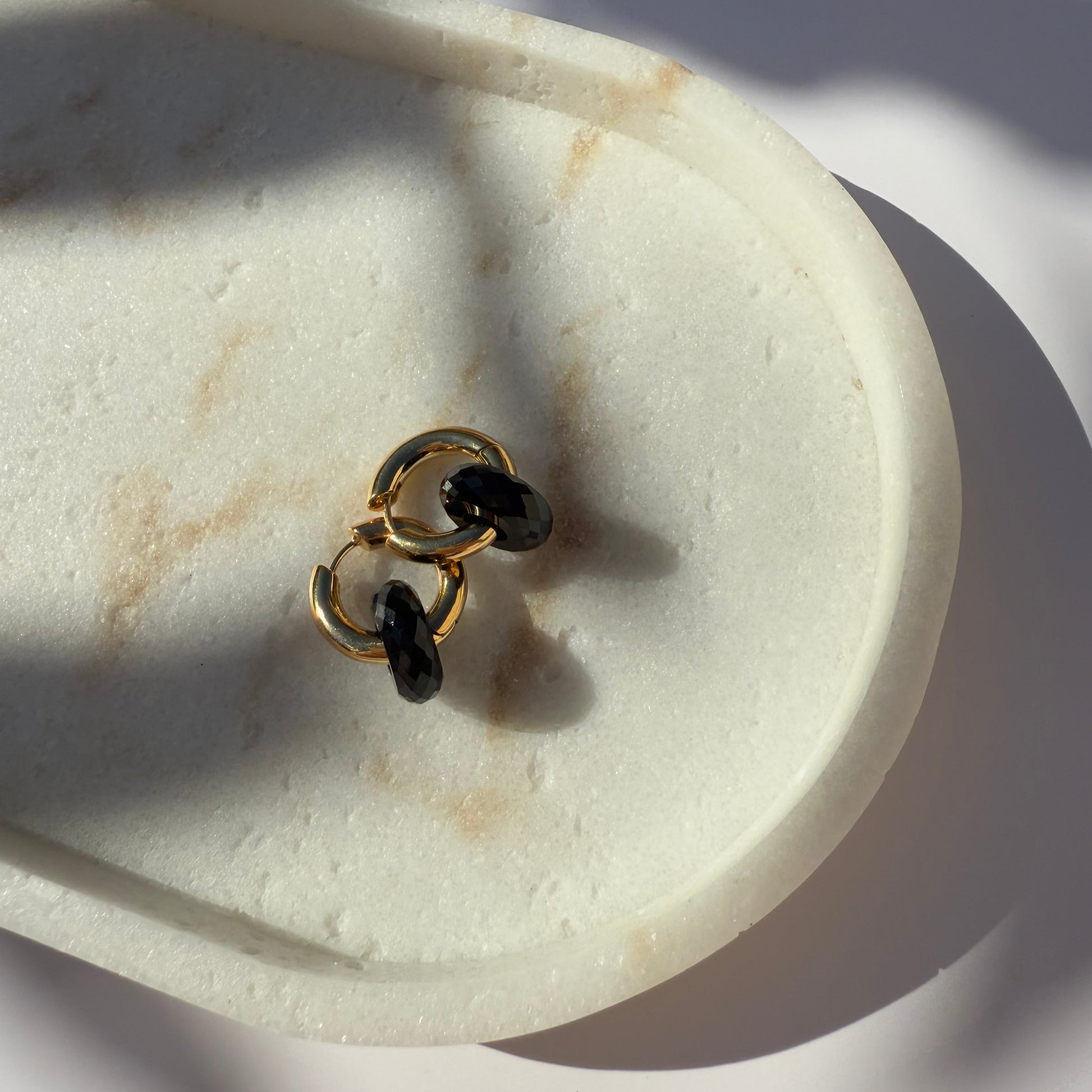 Pair of gold black onyx hoop earrings on marble stone