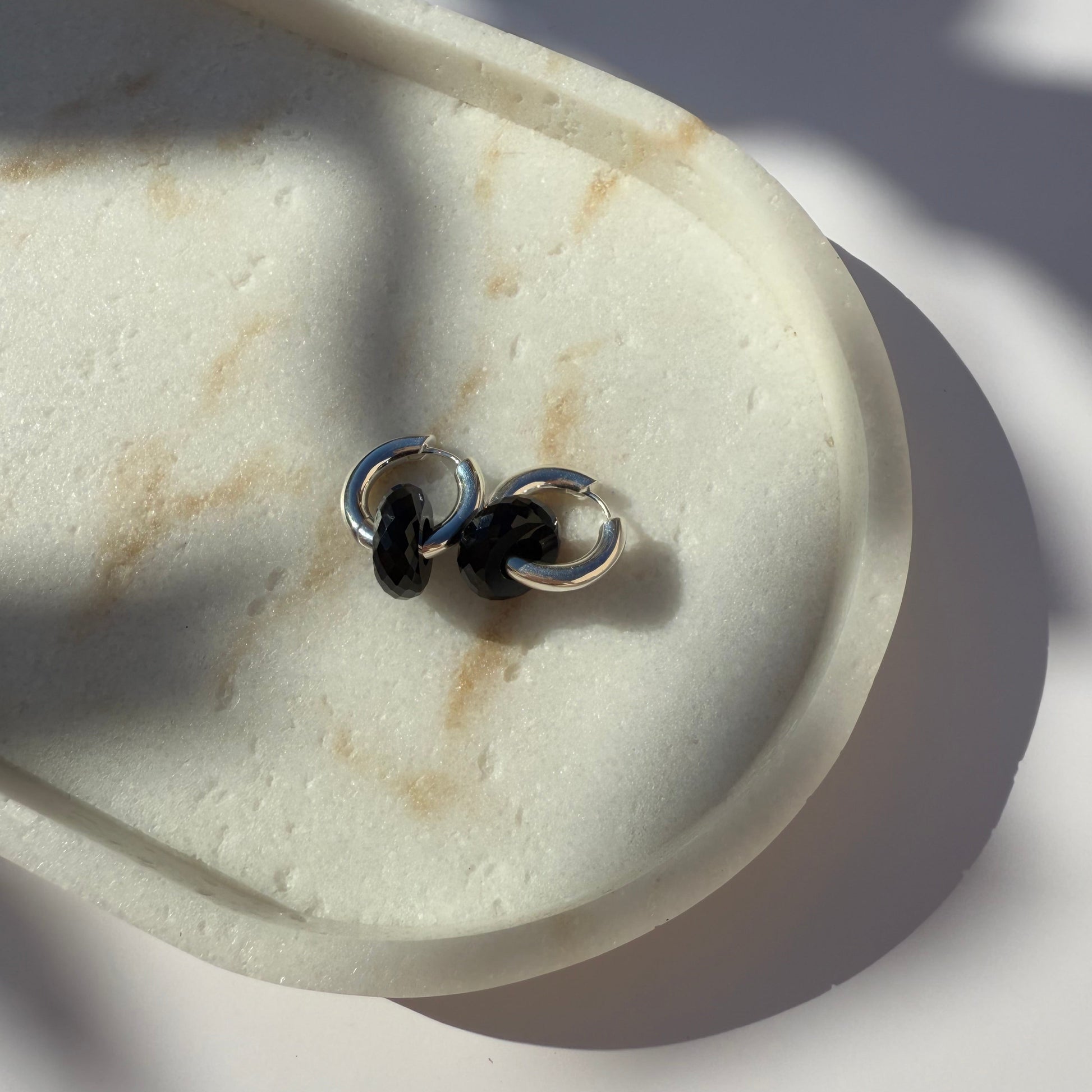 Pair of silver and black onyx hoop earrings on marble stone