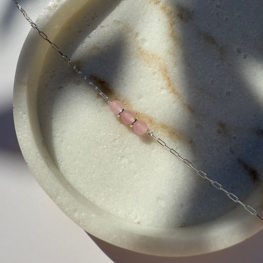 Silver chain necklace with rose quartz beads on marble surface