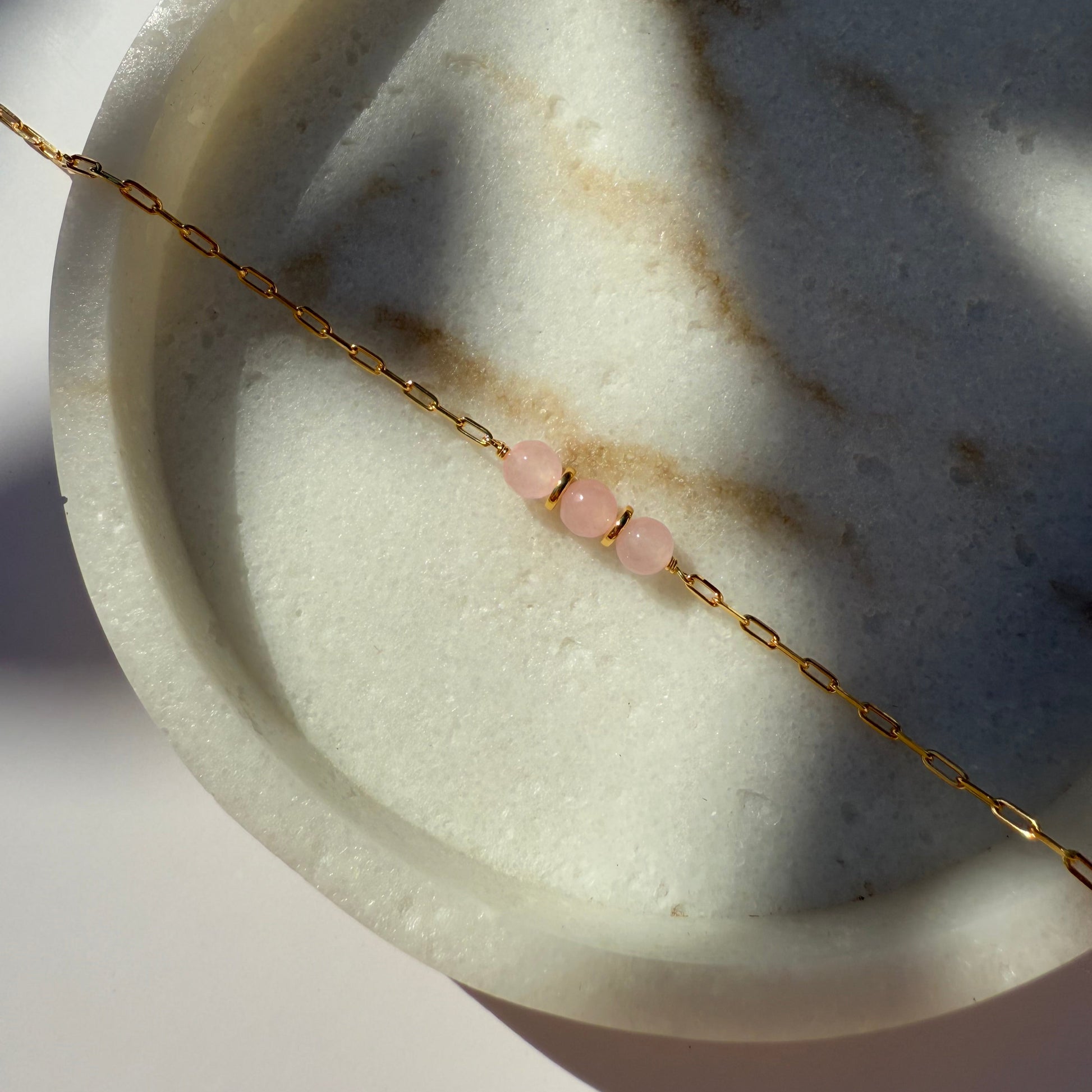 Gold necklace with rose quartz beads on a marble surface