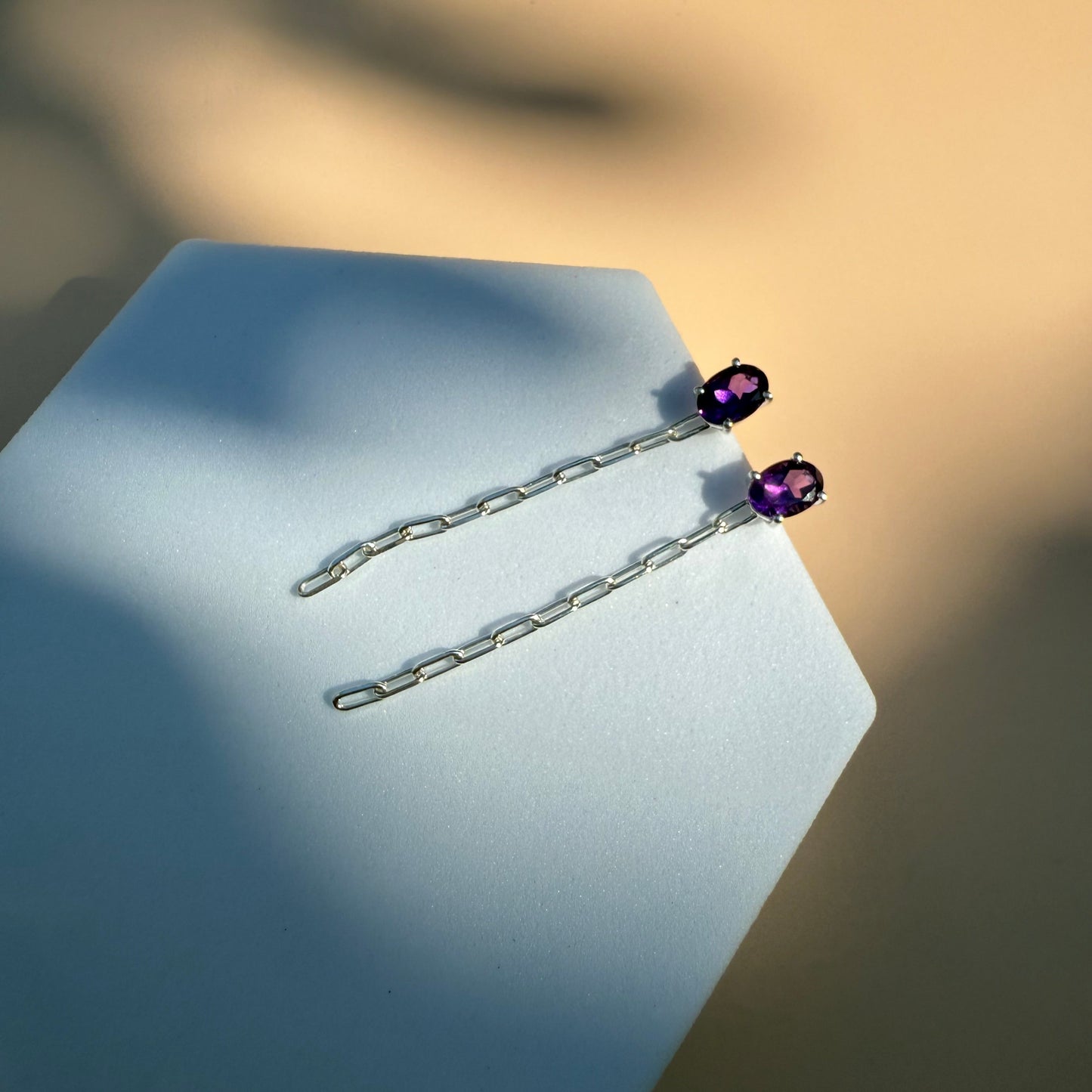 Silver amethyst earrings with dangling chain on a white hexagon 