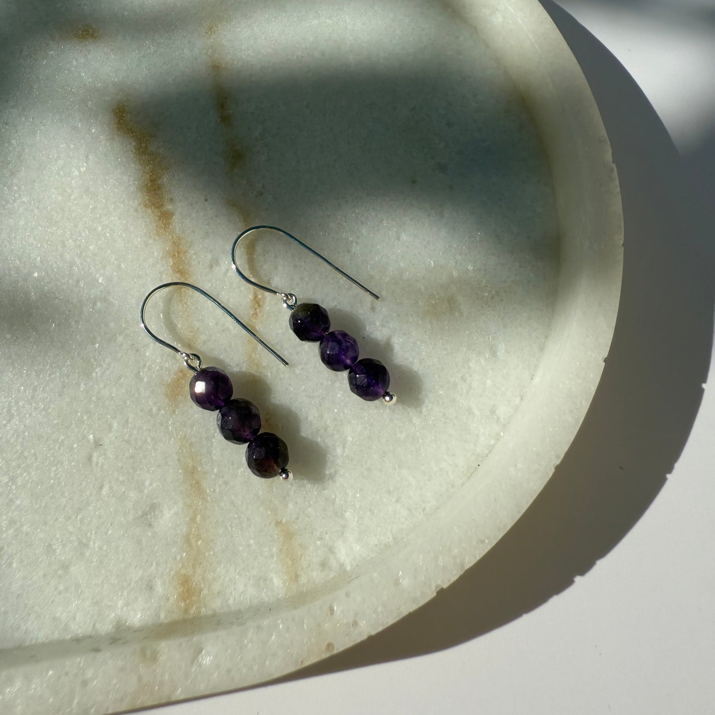 Pair of silver amethyst beaded earrings on a marble surface