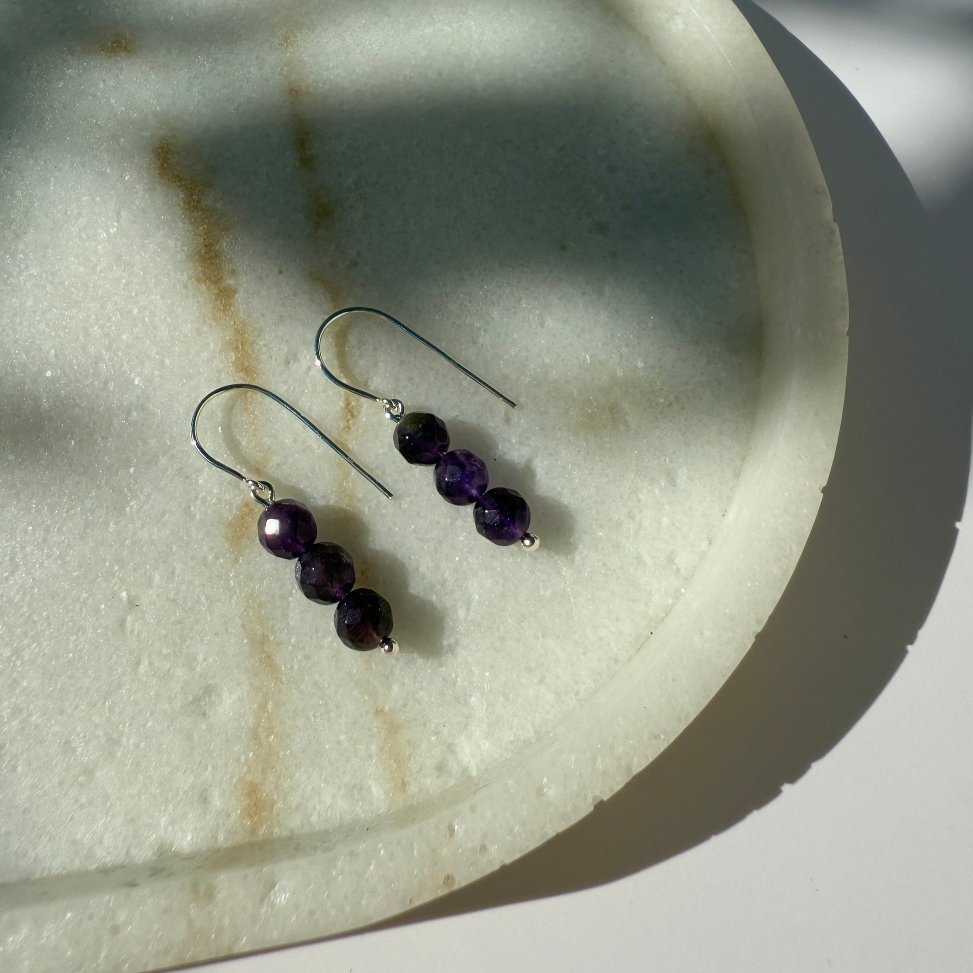 Pair of silver amethyst beaded earrings on a marble surface