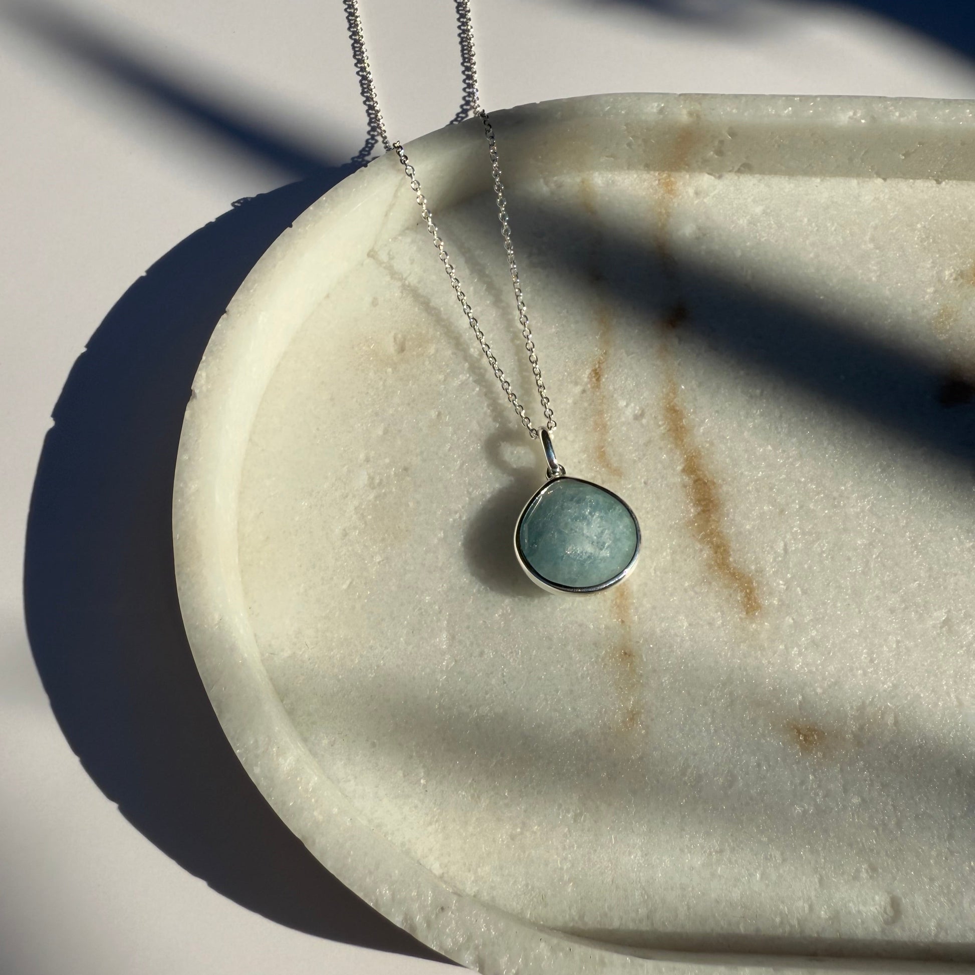 Silver aquamarine necklace with a pear pendant on a marble surface