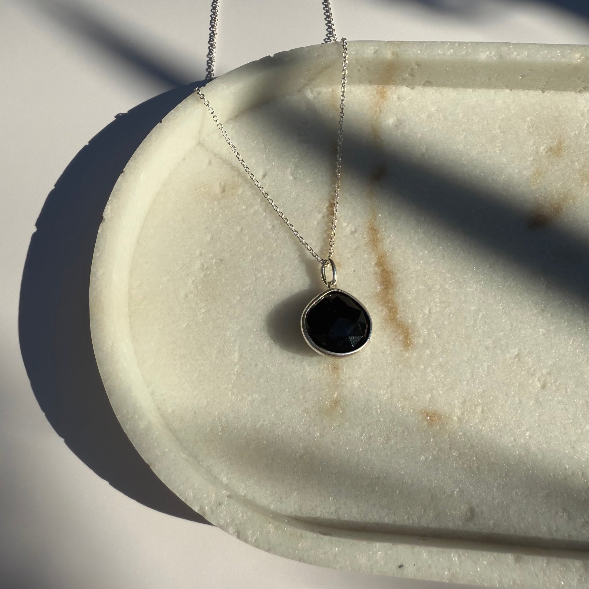 Silver black onyx necklace with a pear pendant on a marble surface