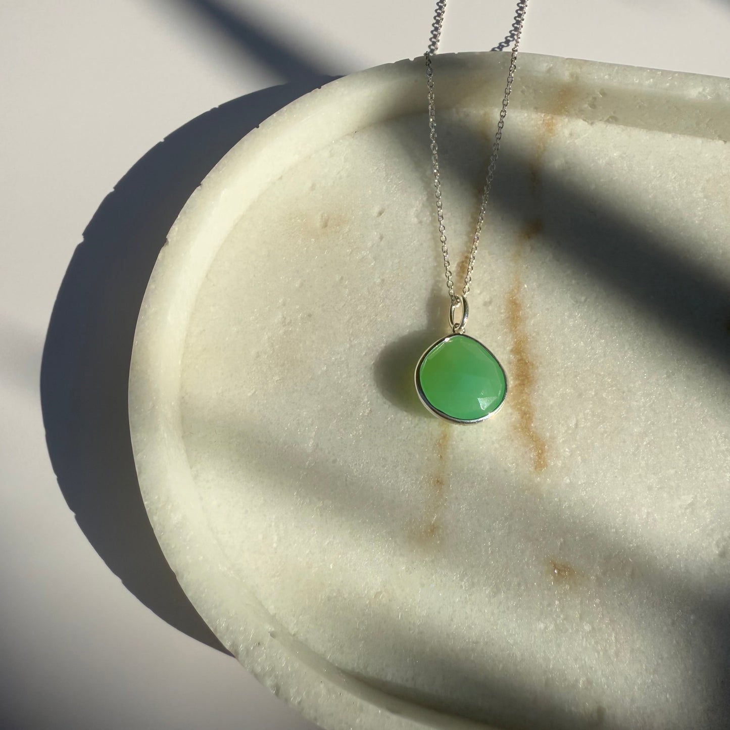 Gold chrysoprase necklace with a pear pendant on a marble surface