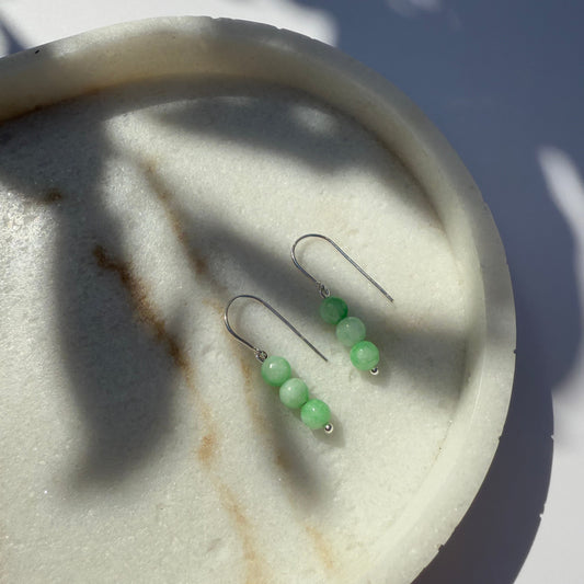 A pair of silver chrysoprase earrings on a marble surface