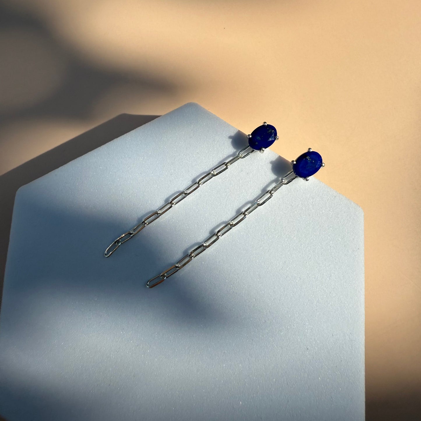 Silver lapis lazuli earrings with dangling chain on a white hexagon 