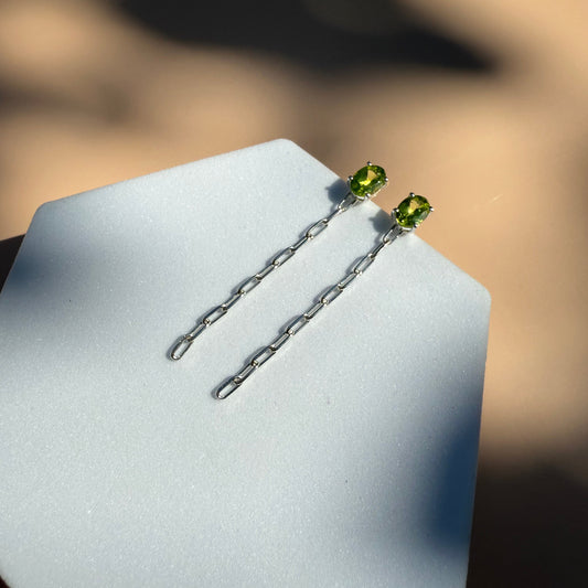 Pair of silver green peridot earrings on a white hexagon