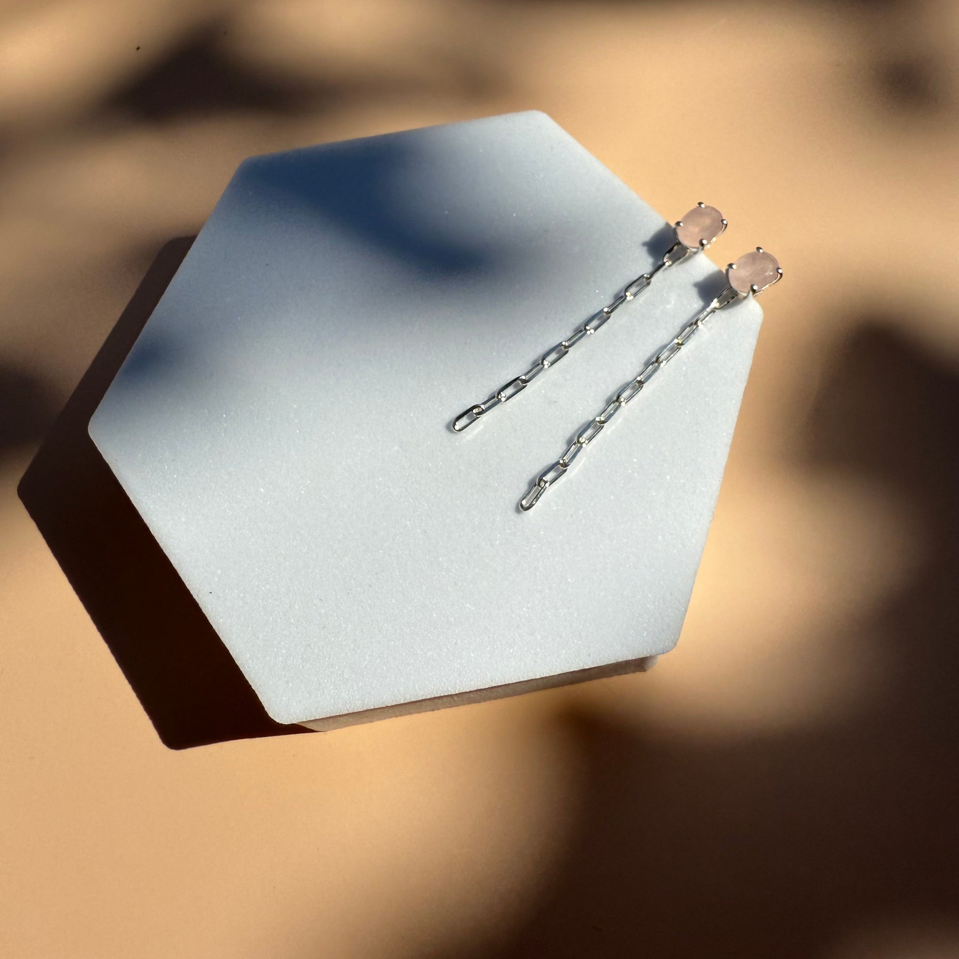 Silver rose quartz earrings with dangling chain on a white hexagon 