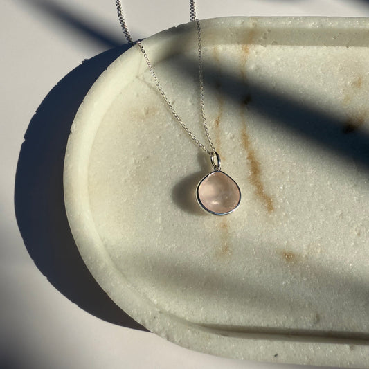 Silver rose quartz necklace with a pear pendant on a marble surface