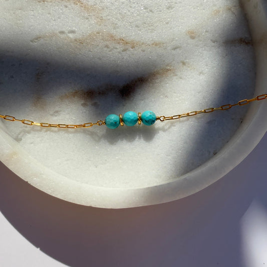 Gold necklace with turquoise beads on a marble surface